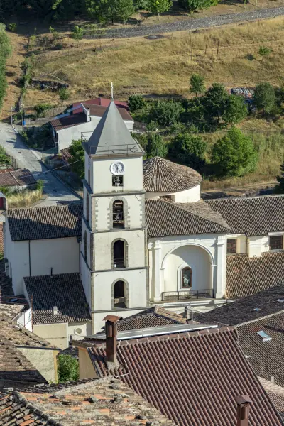 Il campanile con l’orologio e l’abside della chiesa fra i tetti in pietra del centro storico di Calvello