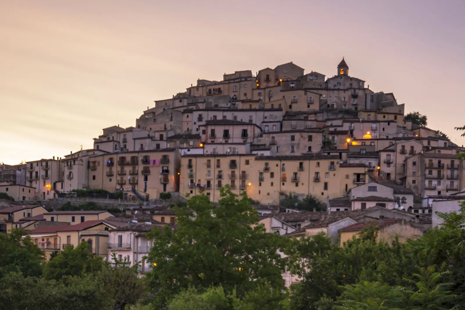 Calvello al crepuscolo: le case del borgo lucano illuminate sulla collina, con il campanile in cima