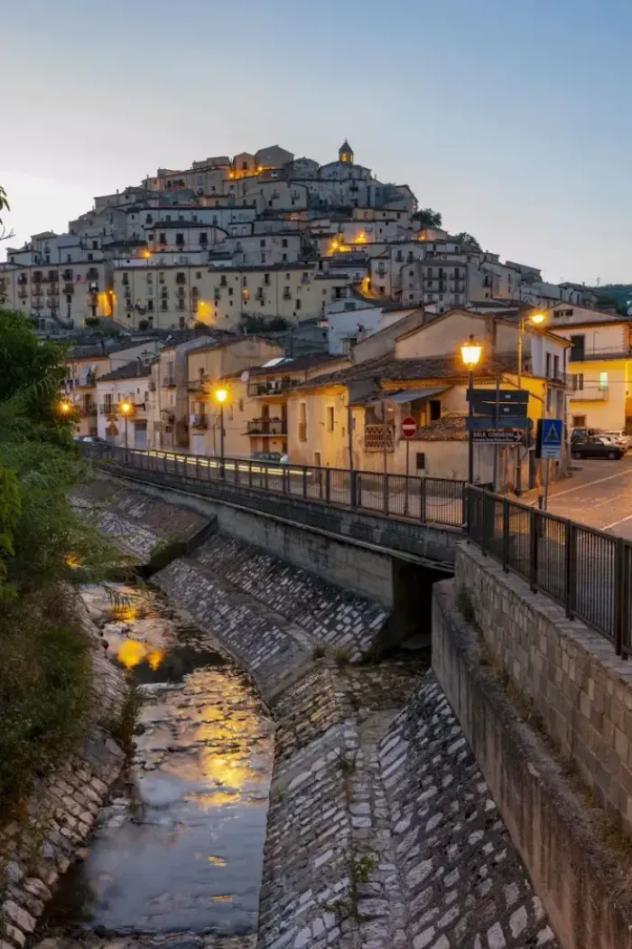 Calvello all’imbrunire visto dal torrente, con le luci accese lungo le case addossate alla collina