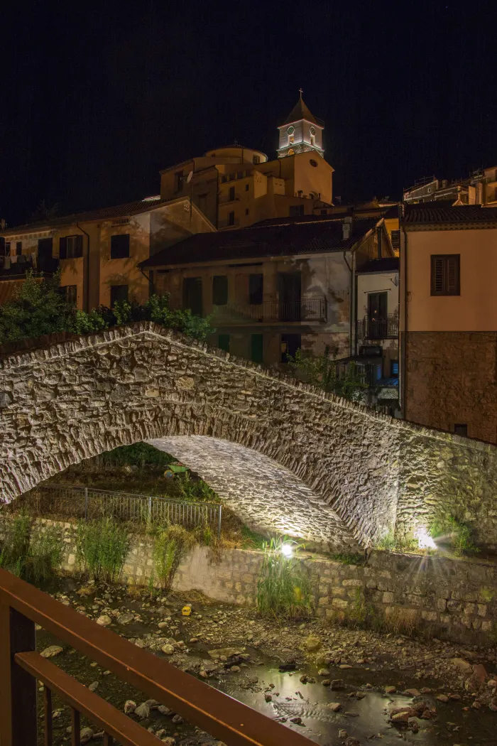 Il ponte in pietra a schiena d’asino di Calvello illuminato di notte, con il borgo e il campanile sullo sfondo