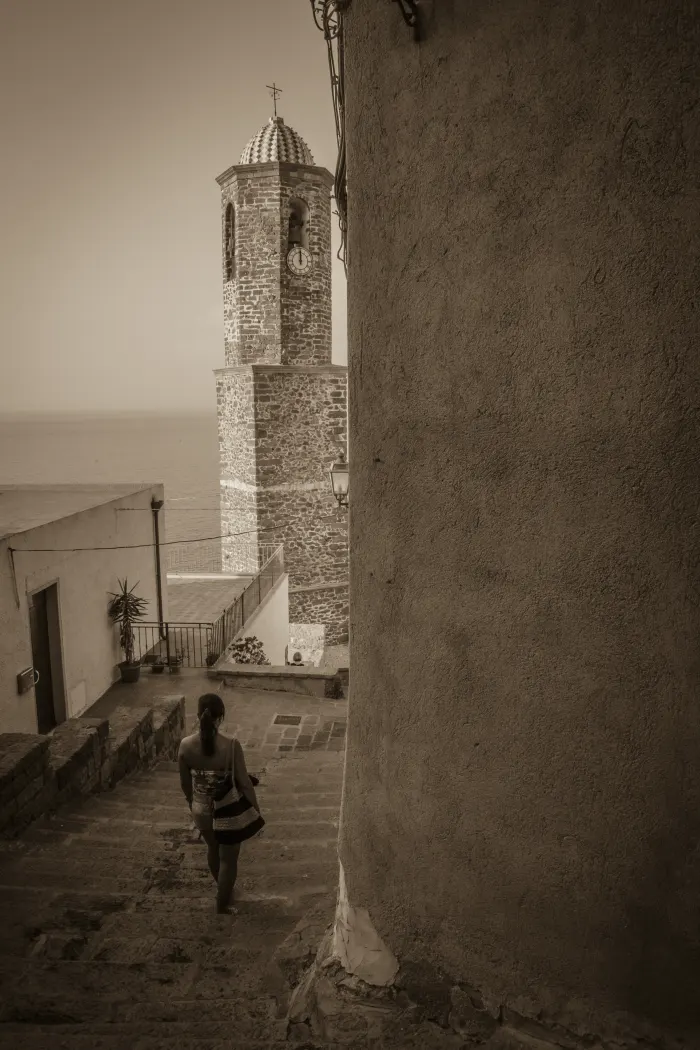 Una scalinata fra le case di Castelsardo che scende verso il mare, con il campanile a cupola maiolicata