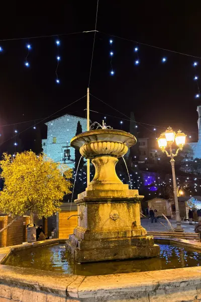 La fontana della piazza di Greccio illuminata dalle luci di Natale, con le casette del mercatino
