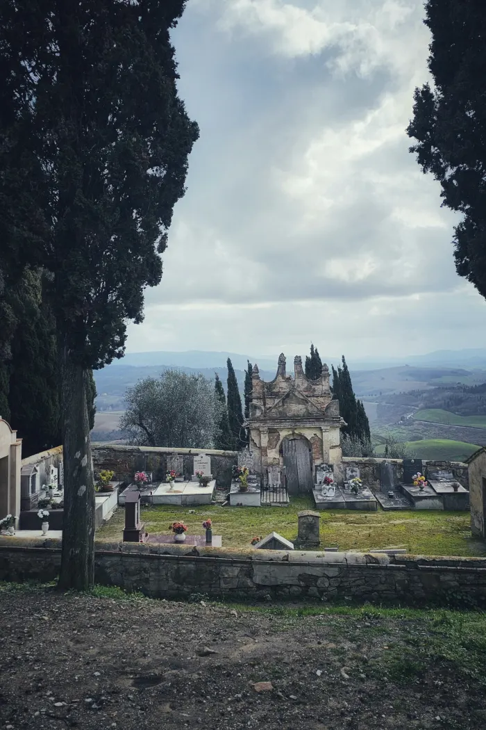 Il piccolo cimitero di Toiano con i cipressi, i fiori sulle tombe e la Valdera sullo sfondo