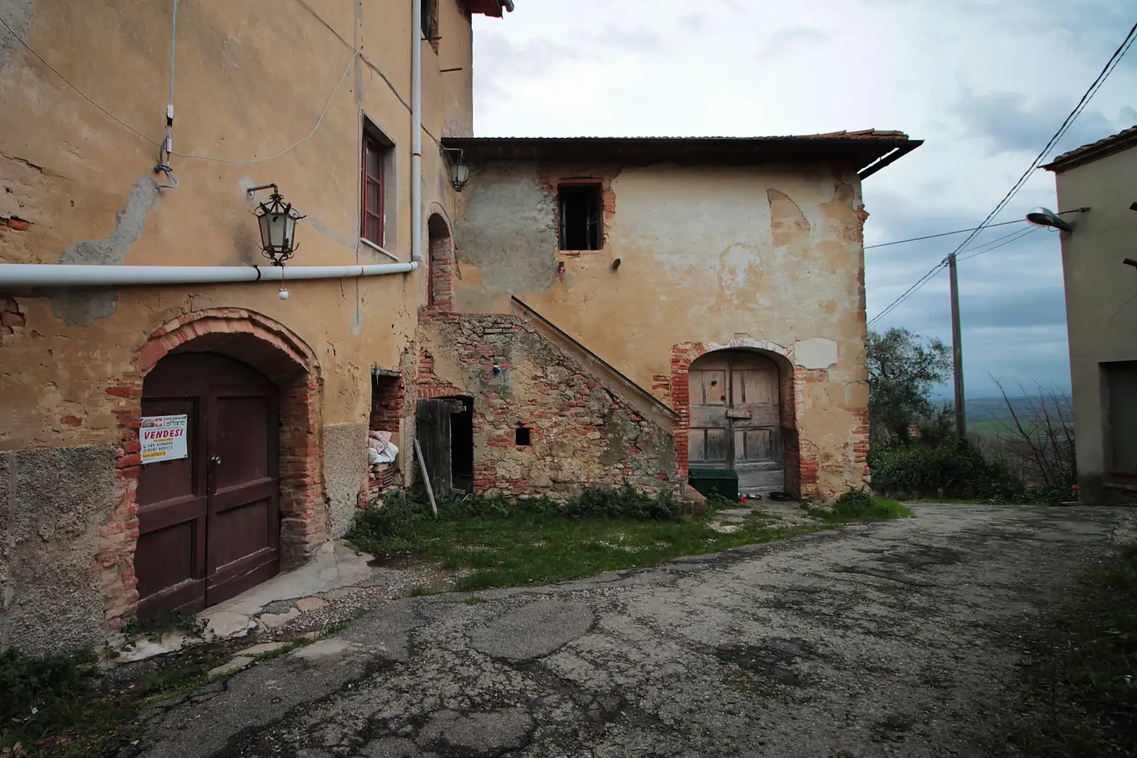Case in pietra e laterizio lungo via del Castello a Toiano, con un cartello Vendesi su un portone